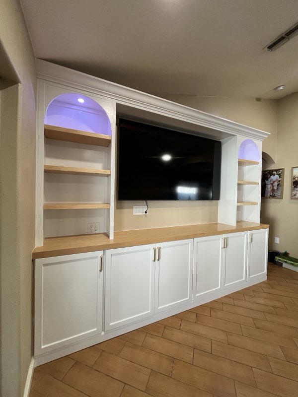 White custom entertainment center with arched LED-lit niches, open wood shelves and shaker cabinets